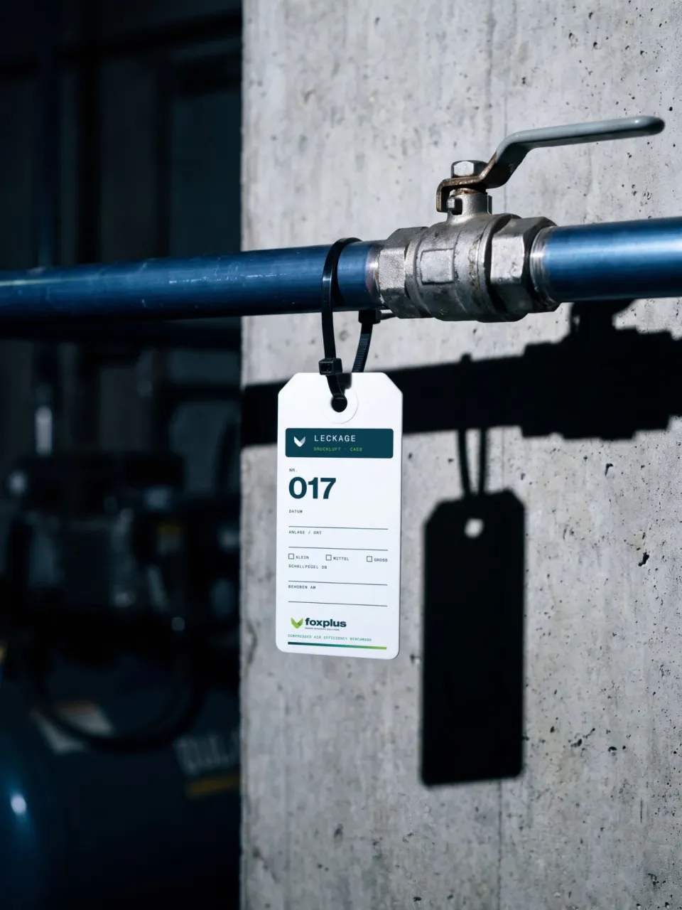 foxplus: leak tag no. 017 fixed with a cable tie to a blue compressed-air pipe next to a ball valve, with fields for date, plant, size and sound level