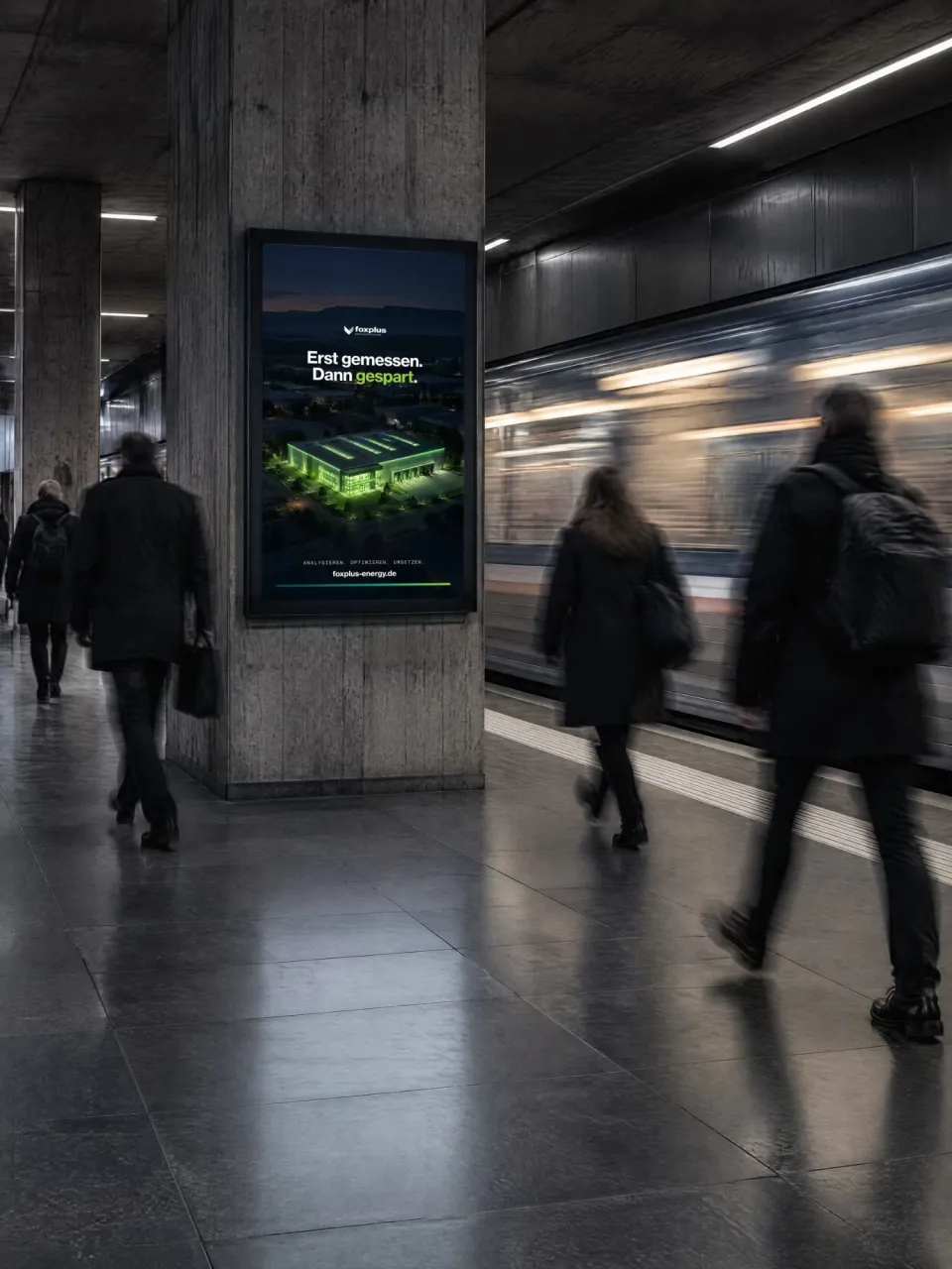 foxplus: digitales Plakat in einer U-Bahn-Station mit nächtlicher Luftaufnahme einer grün beleuchteten Industriehalle und der Zeile „Erst gemessen. Dann gespart.“, davor Pendler und ein einfahrender Zug