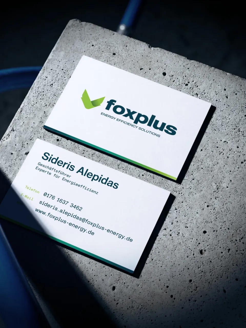 foxplus: two business cards on a concrete block – front with the logo, back with the contact details of Sideris Alepidas, managing director