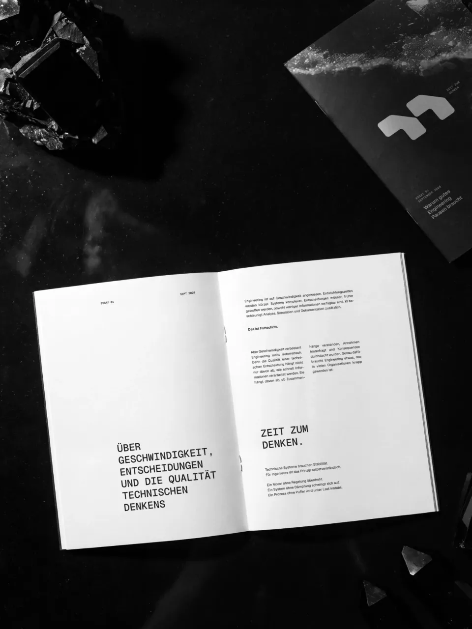 Murugathas: open essay booklet “Über Geschwindigkeit, Entscheidungen und die Qualität technischen Denkens” with the line “Zeit zum Denken.”, beside it the cover with the mark, among black crystals, black and white