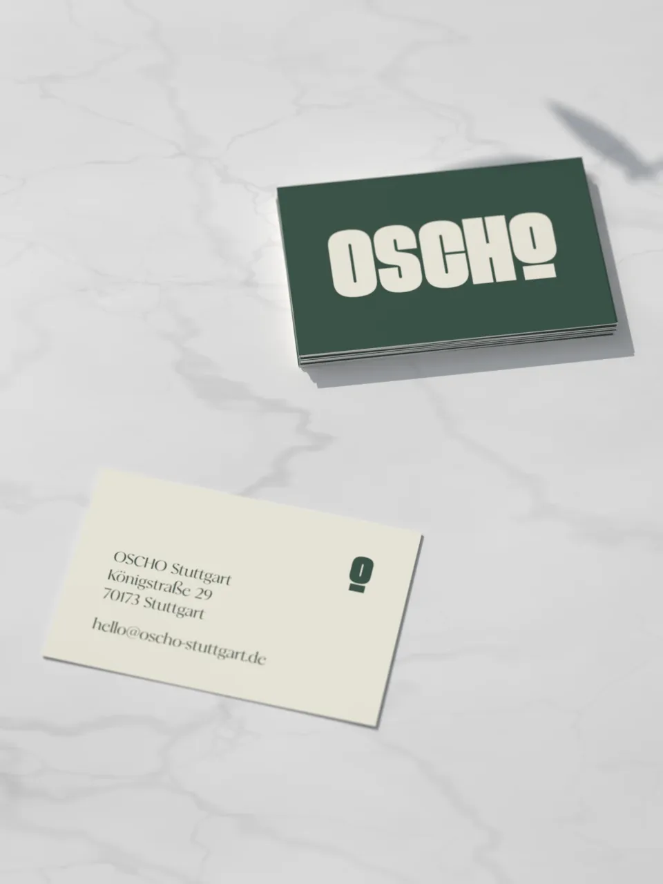 OSCHO: business cards on marble – the cream wordmark on dark green in front, address and logo mark on cream at the back